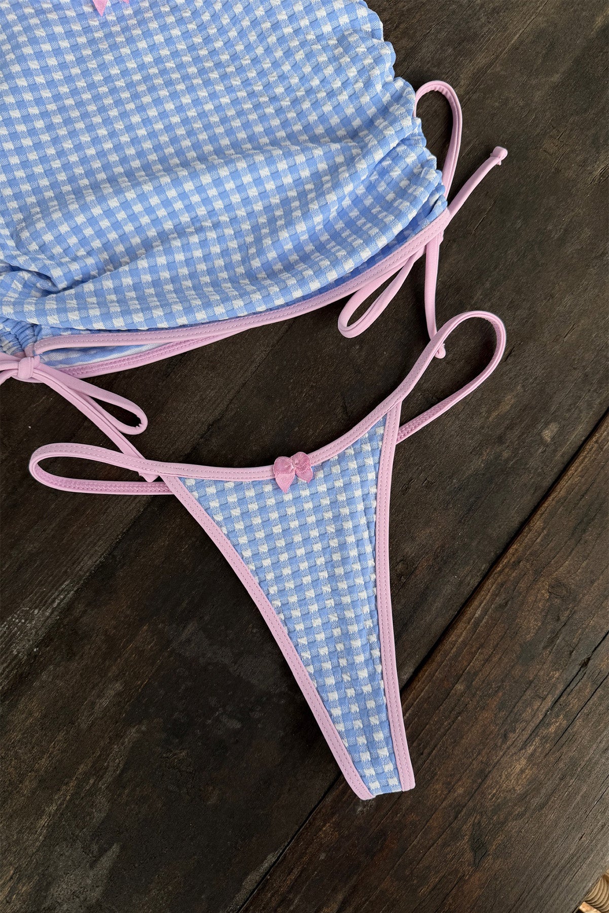 Blue gingham bikini bottom with pink straps on a wooden surface